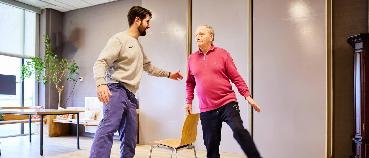 trainer_met_senior_in_roze_shirt_doen_een_balansoefening.jpg