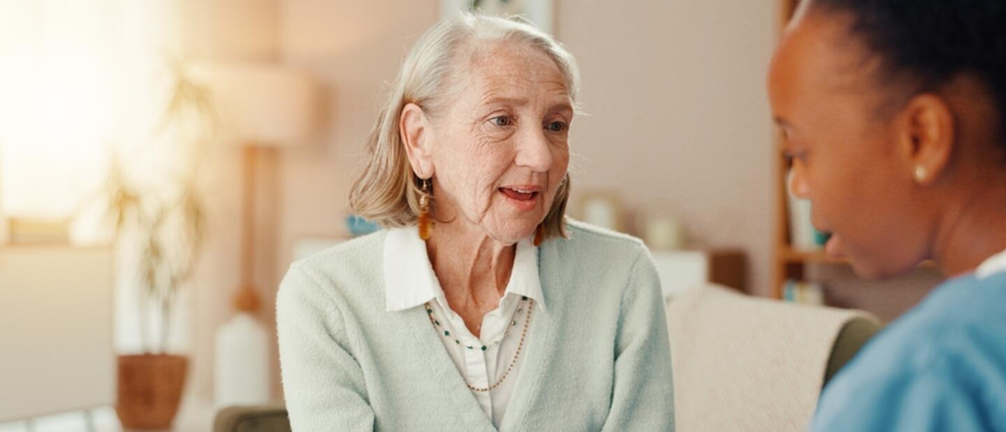 oudere dame met groen vest in gesprek met zorgverlener
