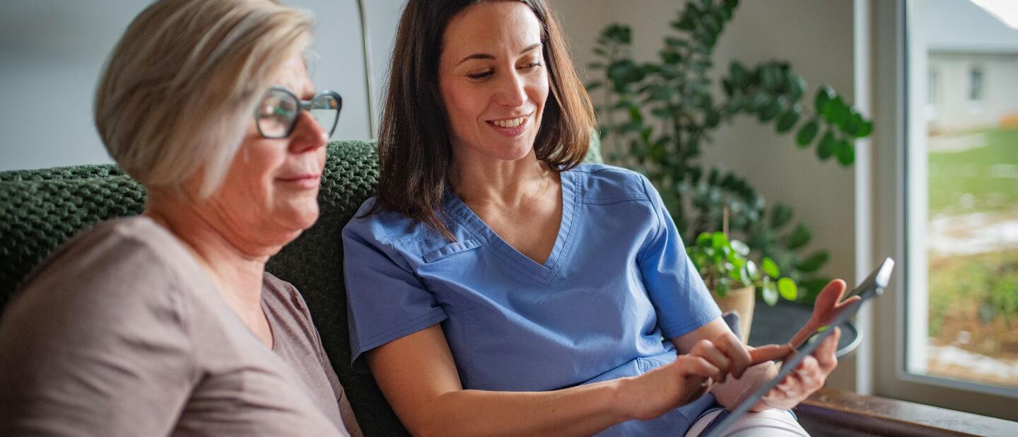senior kijkt met verzorgende naar ipad